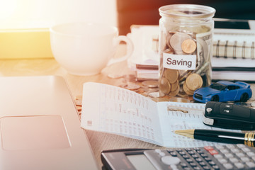 Car insurance and loan concept:Car Key on book bank on desk with Money saving in jar coin bank ,warm tone filter