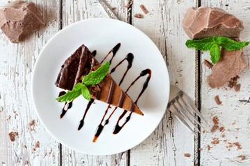 Slice of chocolate cheesecake on plate, above view over a rustic white wood background