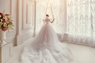Beautiful bride with a long train, standing at the window.