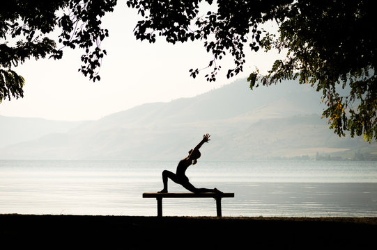 Silhouette of a woman doing low lunge yoga pose on a bench