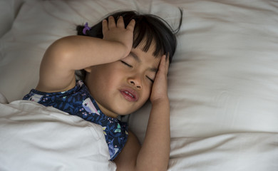 Little Asian girl headache in bed, hands on head