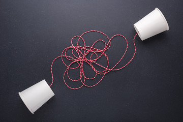 Two white paper cup connect with red rope used for classic phone on black stone table board. For...