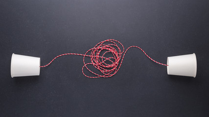 Two white paper cup connect with red rope used for classic phone on black stone table board. For old communication system concept - obrazy, fototapety, plakaty