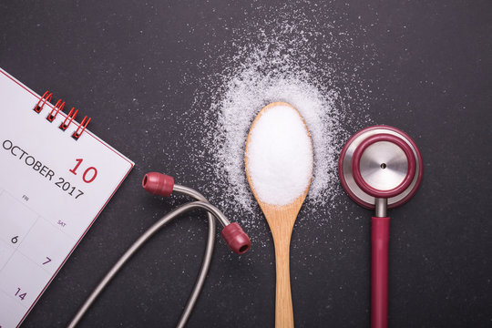 White salt in wooden spoon, calendar and doctor stethoscope on black stone table background. Healthy and kidney concept
