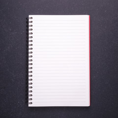 Notebook with blank empty cover on black stone table background. Top view