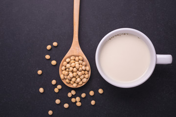 Soy milk in white cup and soy bean on dark table. Top view