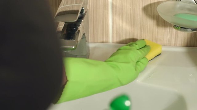 Close-up of female hands wearing protective gloves, cleaning bathroom sink with sponge. Girl washes the sink in bathroom with a washcloth. Slow motion.