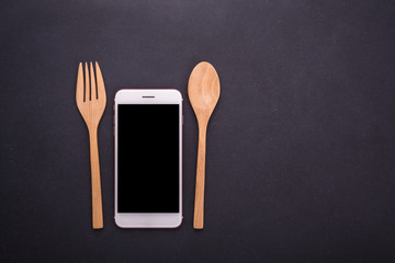 Smartphone, spoon and fork on black stone table background, concept Eating technology