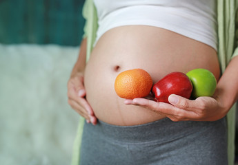 Pregnant woman holding Green-Red Apple and Orange fruit at her tummy. Dieting Concept.