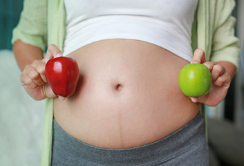 Pregnant woman holding Red-Green Apple fruit at her belly.