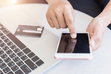 Woman hands holding/using smartphone and credit card in front of laptop on the desk. Easy way online shopping concept.