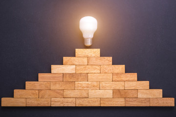 Wooden block set up for staircase with light bulbs on the top point on black stone board. Business...