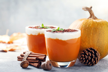 Pumpkin smoothie in glasses with cinnamon and acorns on wooden table