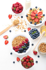 Granola with berries in plate and honey on white wooden table