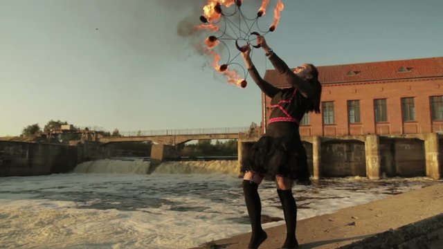 A young girl shows a fire show against the backdrop of an old German hydroelectric power station.