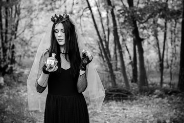 Halloween composition. Beautiful dark haired girl in black dress witches costume with walking in the forest. Halloween Witch in a dark forest. Halloween art design. Background For Halloween Concept