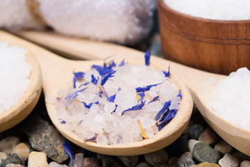 background with sea salt with elements of a blue flower, in a wooden spoon
