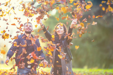 Young lovely happy couple -  lovers flying with leaves  in autumn park