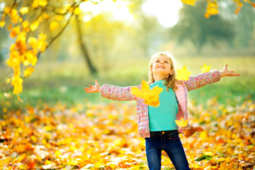 happy young girl in a beautiful autumn park playing under falling leaves.