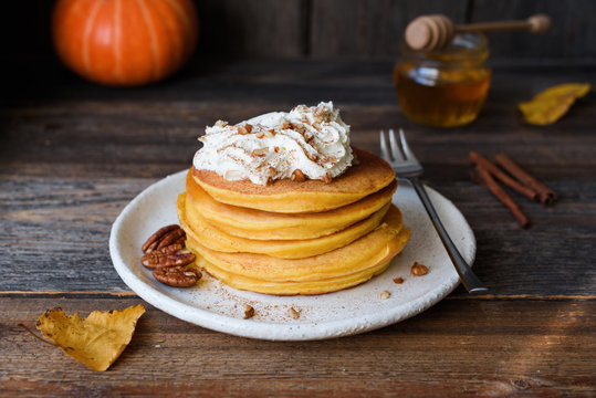 Pumpkin pancakes with whipped cream and cinnamon on old wooden table. Autumn comfort food, breakfast food