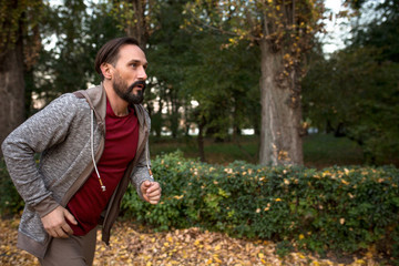 Side view of man running in autumn forest. Healhy male doing cardio workout jogging in city park.