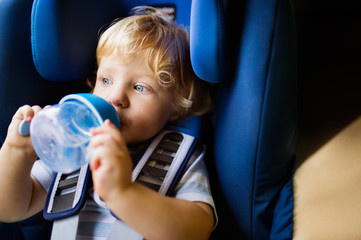 Little boy sitting in the car seat in the car, drinking.