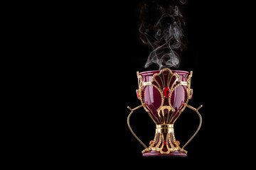 Red And Gold Arabic Traditional Incense Bukhoor Agar Wood Burner In A Mabkhara With Smoke Isolated On Black Background. Used In Majlis, Ramadan And Eid Occasions. Blank Text Space