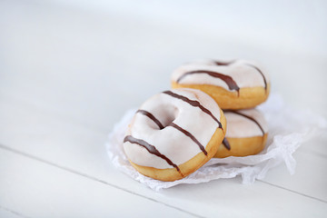 Donut. Three white striped donuts on white  paper on a  wooden plank background