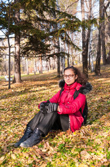 Fototapeta na wymiar Beautiful girl in a red jacket sits in an autumn forest