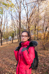 Fototapeta na wymiar Beautiful girl in a red jacket with a backpack stands in the autumn forest