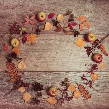 Autumn arrangement of leaves, apples and berries on a wooden background with free space for text. Top view, season concept, toned retro effect