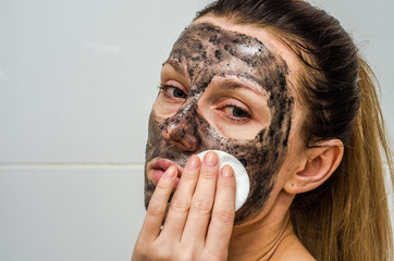 Young charming girl makes a black charcoal mask on her face