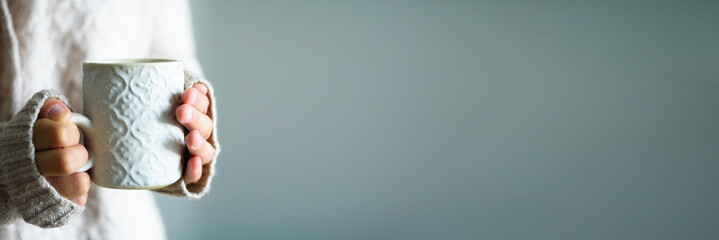 Famale hands holding a cozy ceramic handmade mug with coffe. Winter and Christmas home time concept. Lifestyle. Copy space. Banner