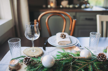 Festive Christmas and New Year table setting in scandinavian style with rustic handmade details in natural and white tones. Dining place decorated with pine cones, branches and candles