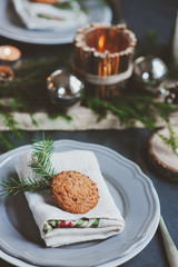 Festive Christmas and New Year table setting in scandinavian style with rustic handmade details in natural and white tones. Dining place decorated with pine cones, branches and candles
