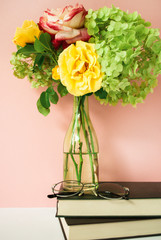 Beautiful bouquet of flowers in glass vase on a stack of books in front of pale pink pastel background