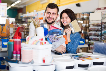 smiling loving couple demonstrating tools for house renovating in paint store