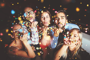 Group of people having a party, blowing confetti  - obrazy, fototapety, plakaty