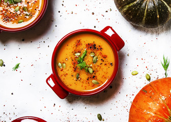 Spicy pumpkin soup in red pan, white background, top view