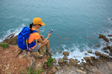 Young woman hiker using smartphone sit on seaside cliff