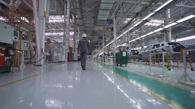 Automobile plant, modern production of cars, robot equipment, working man walks near the automated production line.
