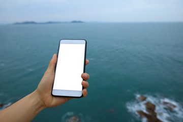 Hand using smartphone with sea and sky on the background