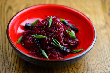 Beetroot salad in a red bowl on a wooden background, sprinkled with finely chopped onion