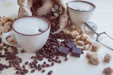Two cups of freshly brewed, frothy cappuccino. Spilled coffee grains, chocolate and cane sugar. Theme of coffee, cappuccino, mocha chino, america no. Beautiful elegant background with place for text