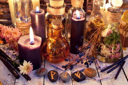 Magic runes, black candles, flowers and berries on witch table in candle light