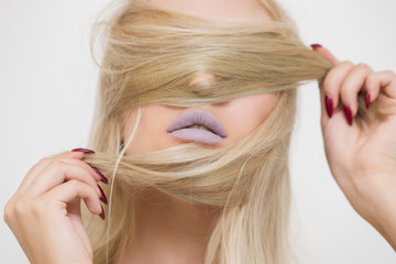 Fototapeta premium Beautiful blonde girl closes her eyes and chin hair. Is the lipstick, the hair. Makeup, cosmetics, skin care
