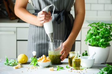Woman using hand blender to make pesto. White kitchen interior design. Copy space. Vegetarian,...