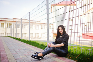 Fashion outdoor photo of gorgeous sensual woman with dark hair in elegant clothes sitting against iron fence at autumn city.