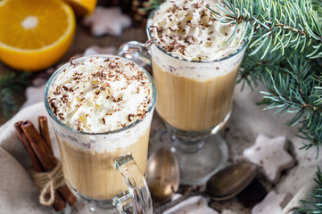 Christmas background with two latte, cookies star, fir branches, cones, orange and spices, close up. Couple coffee with milk and homemade tasty cookies in tray on wooden background. Top view.