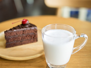 glass of milk with chocolate cakes on top red cherry background in wooden plate on wood table